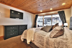 Een slaapkamer met een groot bed, een aan de muur bevestigde televisie, een dressoir en een raam met gordijnen.