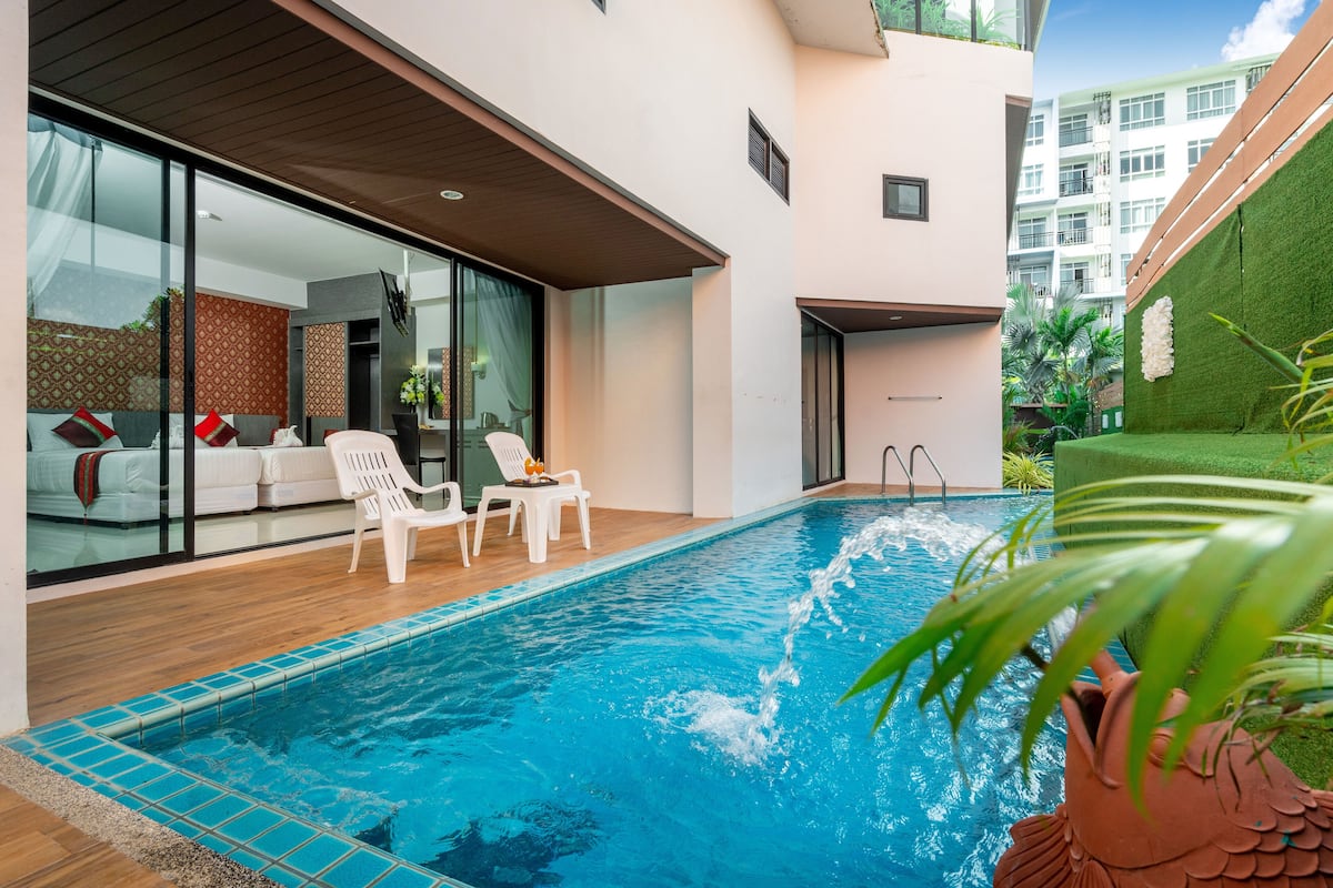 Piscina interior moderna con agua azul cristalina, rodeada por una terraza de madera y sillones blancos.