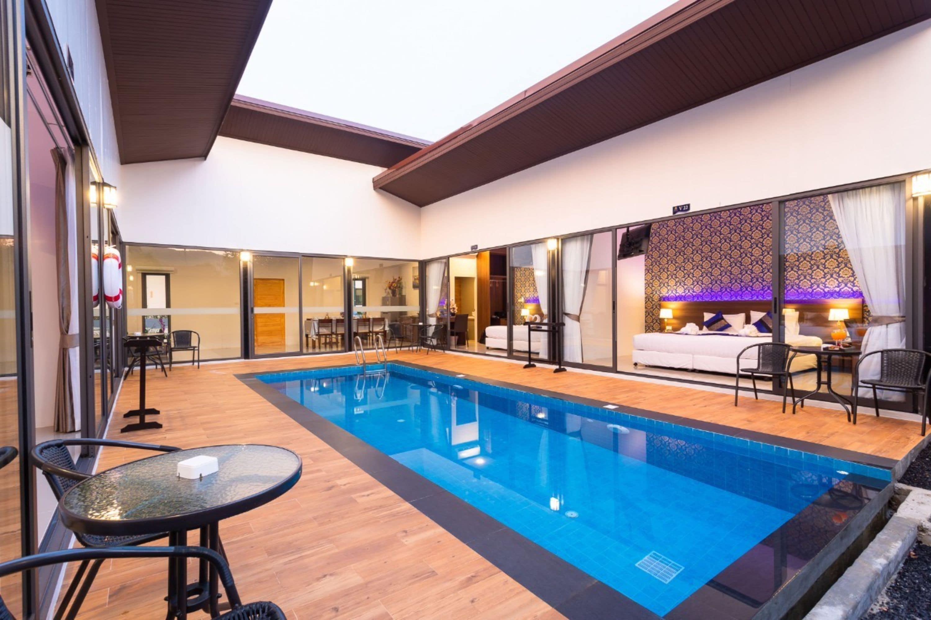 A modern indoor pool area with a glass wall, wooden flooring, and a seating area with tables and chairs.
