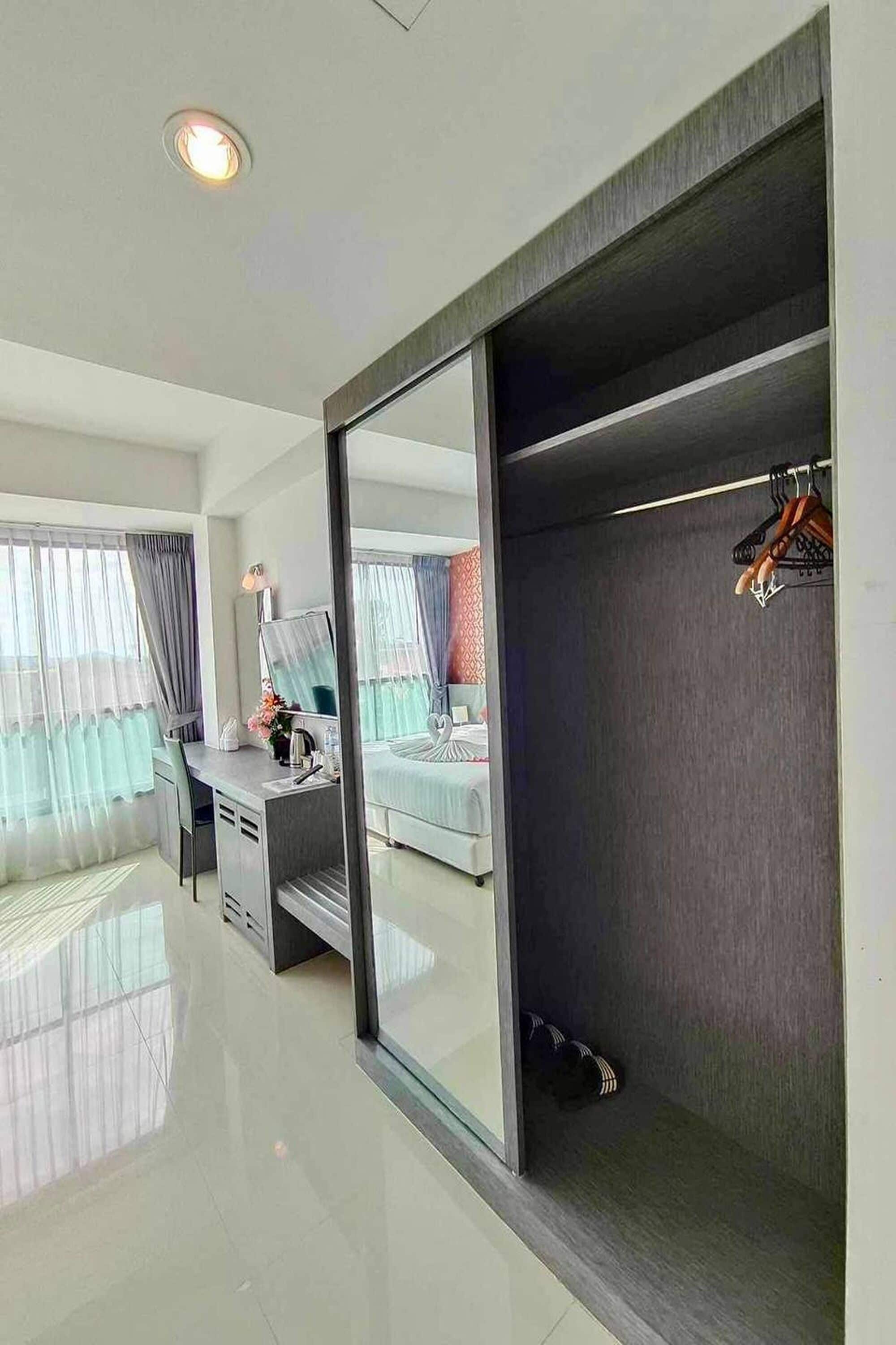 A modern hotel room with a bed, a desk, a chair, a wardrobe, and a mirror.