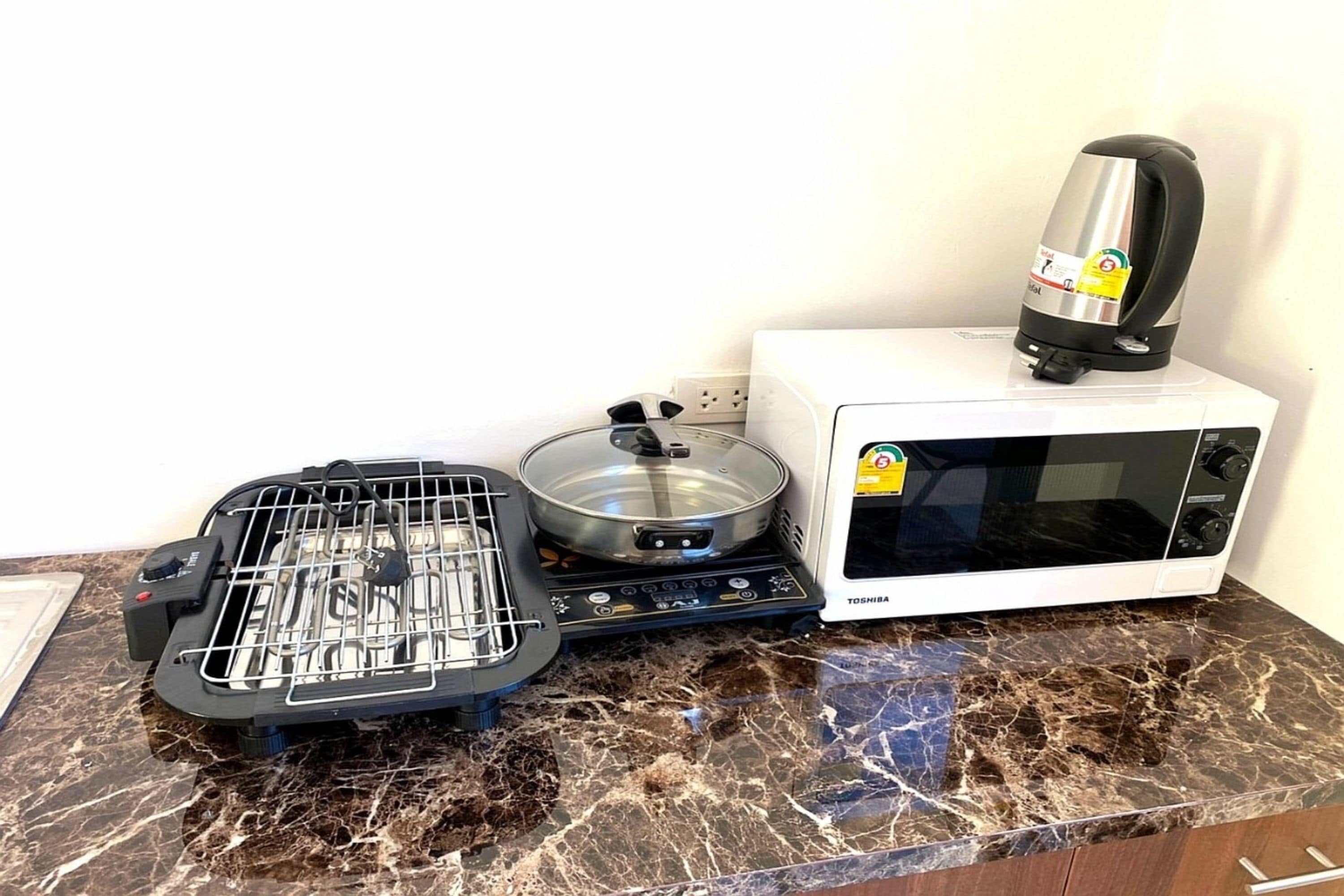 A kitchen with a stove, a microwave, and a kettle on a marble countertop.