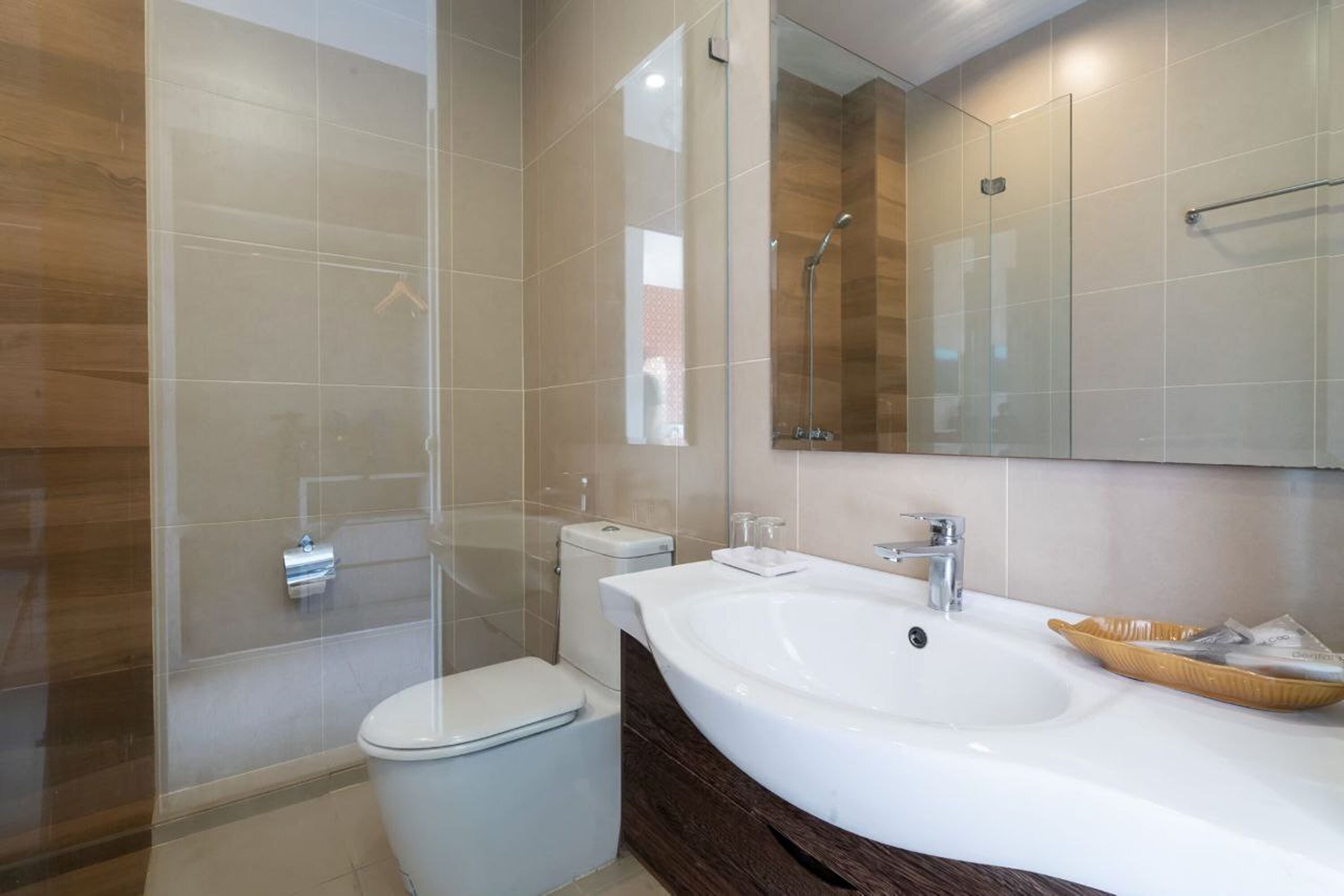 Un baño moderno con cabina de ducha de vidrio, inodoro blanco, tocador con lavamanos grande y espejo.