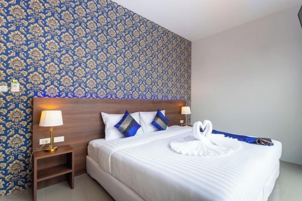 A hotel room with a patterned wallpaper, a neatly made bed with white bedding and blue pillows, and two bedside lamps.