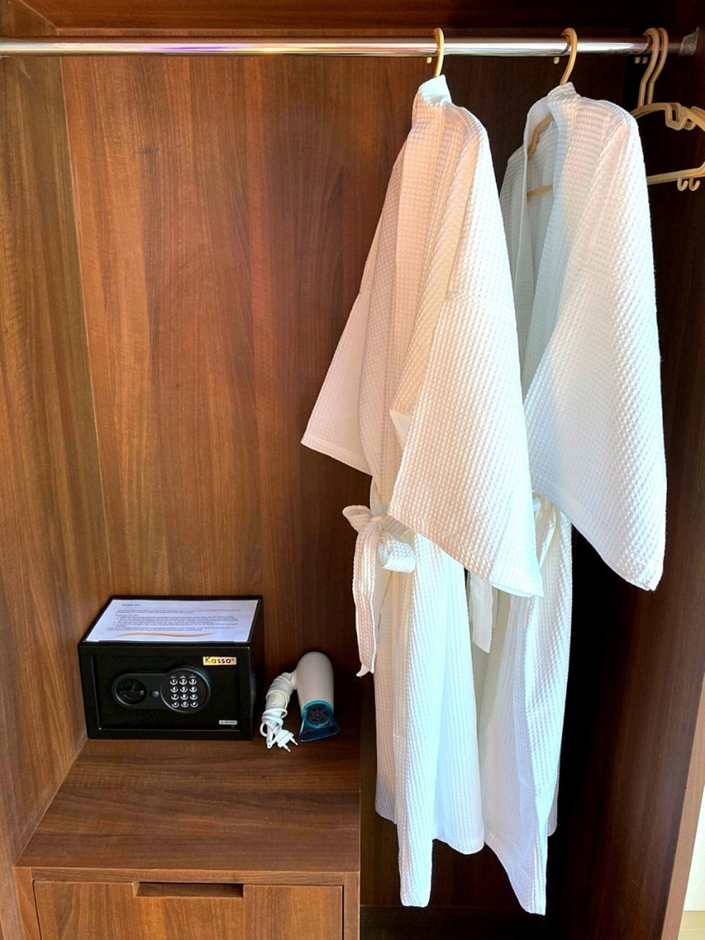 Un placard en bois dans lequel sont suspendues deux robes blanches sur une tringle, une radio noire et un sèche-cheveux blanc posés sur une étagère.