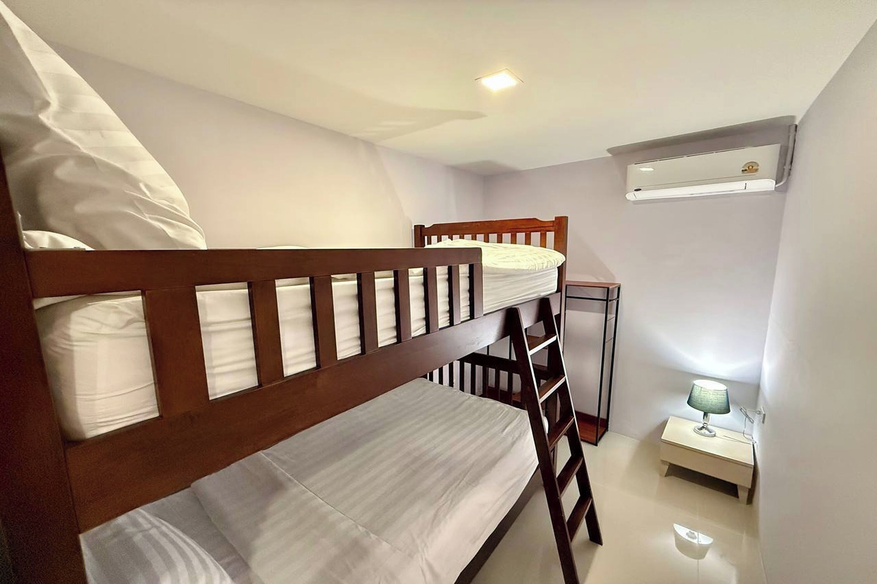 A bunk bed room with a ladder, a bedside table with a lamp, and an air conditioning unit on the wall.