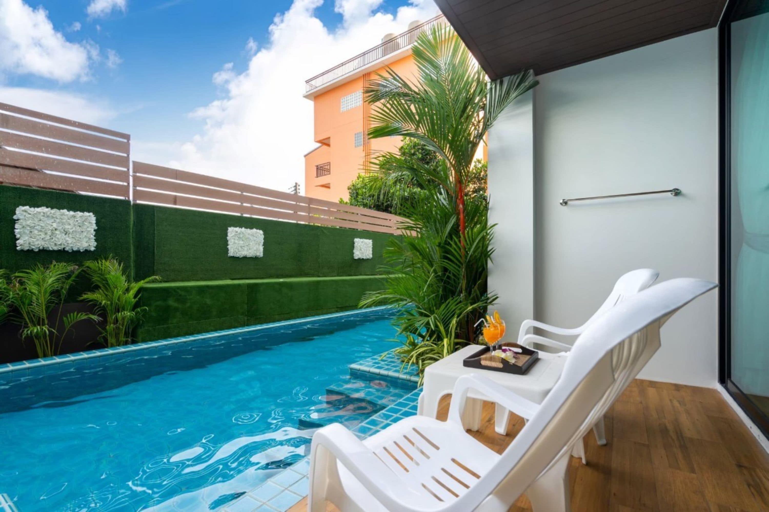 Zona de piscina con una silla de descanso blanca, una mesita con una bebida y vistas a un edificio con balcón.