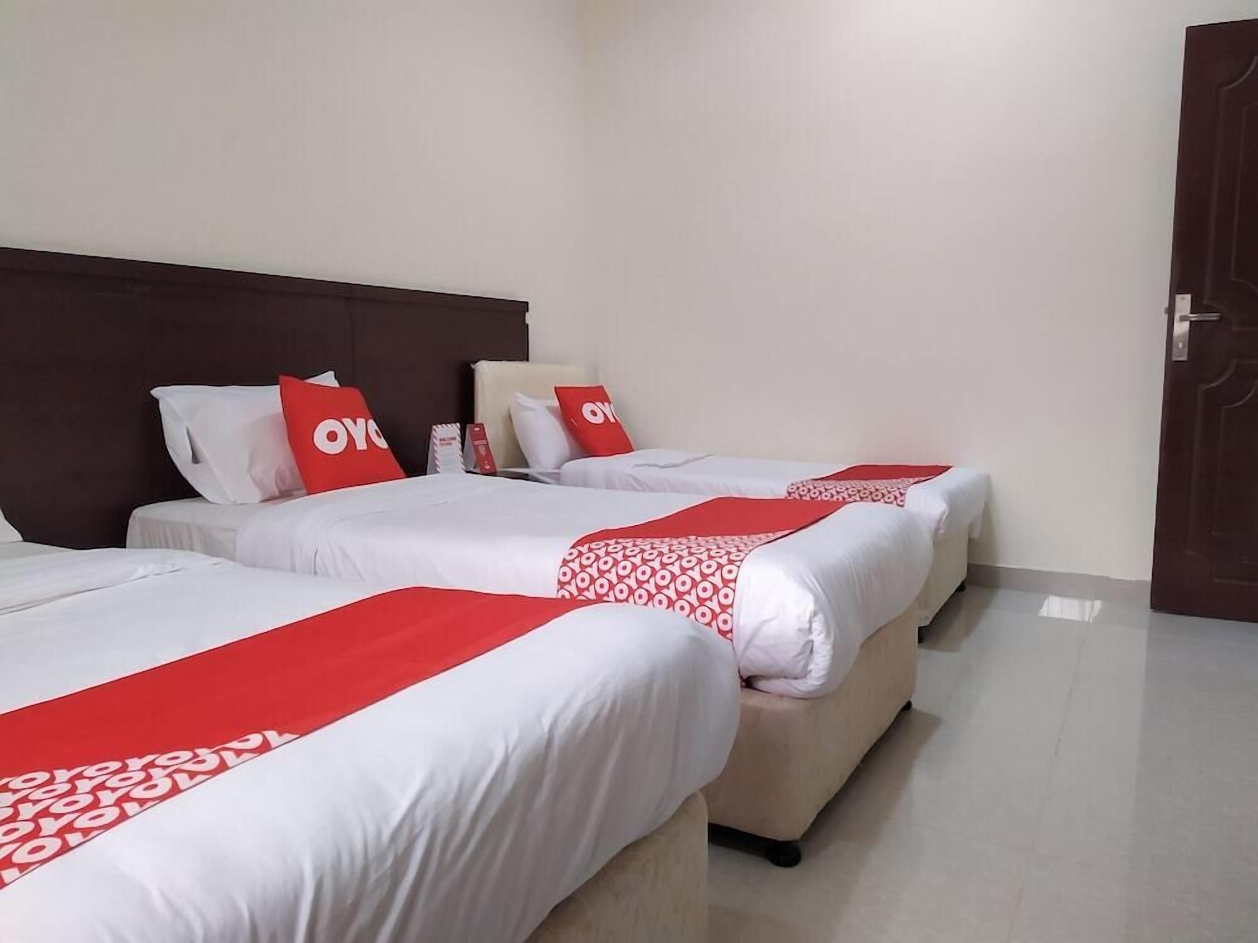 A hotel room with three beds, each with white bedding and red accents.