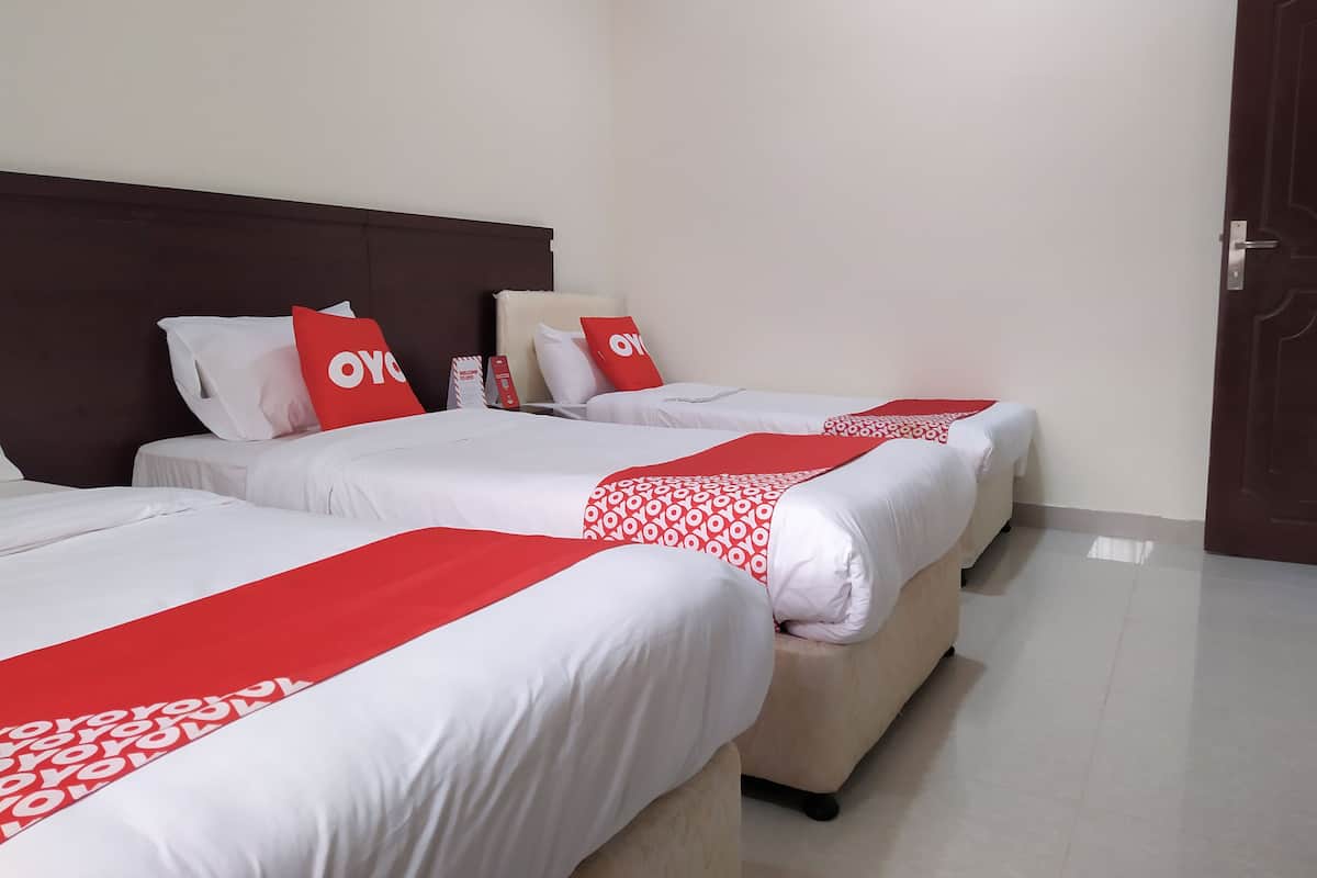 Une chambre d’hôtel avec trois lits, chacun agrémenté de draps blancs et de touches de couleur rouge.