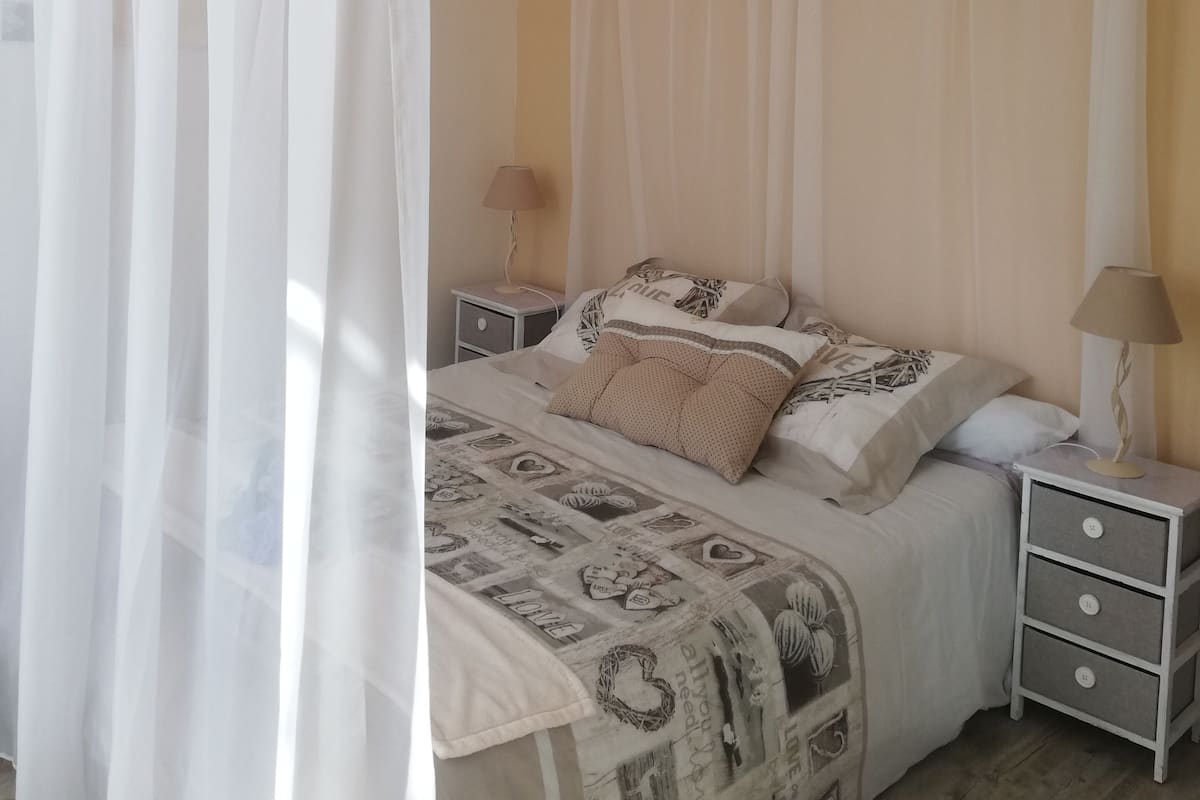 Een slaapkamer met een hemelbed, twee nachtkastjes met lampen en een bed met een versierde spreideken.