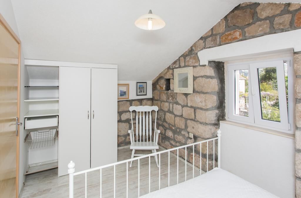 A room with a stone wall, a white chair, a window, and a white wardrobe.