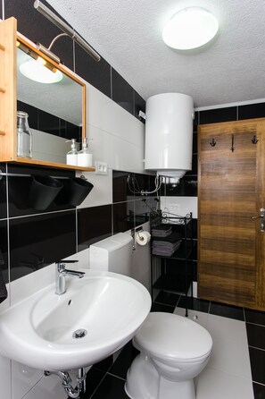 A modern bathroom with a white sink, toilet, and a wooden door. - Apartments Heart of Dubrovnik (Dubrovnik)