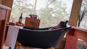 A bathtub with gold claw feet, a bottle of wine, and a candle on a wooden table. - Asanja Grumeti (Serengeti)