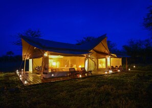 A tented accommodation with a wooden deck, outdoor seating, and ambient lighting.