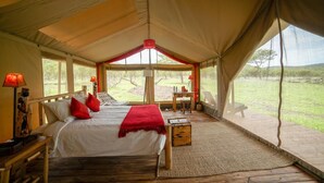 A tented room with a bed, two bedside tables, a red throw blanket, and a view of the outdoors. - Asanja Grumeti (Serengeti)