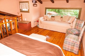Una habitación acogedora con suelo de madera, un sofá con cojines a rayas, un sillón escocés y un ventanal con vistas al verdor.