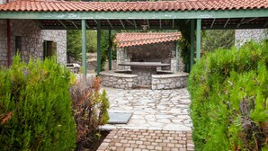 Une terrasse en pierre avec une structure de toit en tuiles, entourée de verdure.