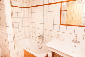 Un baño con paredes de azulejos blancos, una bañera, un lavabo y un espejo.