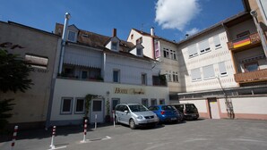 A hotel with a white facade, multiple windows, and a sign reading "Hotel Amadeus." There are cars parked in front, and a clear blue sky above. - Hotel Amadeus (Speyer)