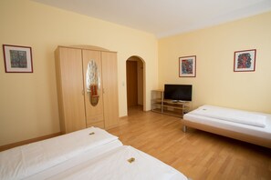 A hotel room with two single beds, a wardrobe, a television, and artwork on the walls. - Hotel Amadeus (Speyer)