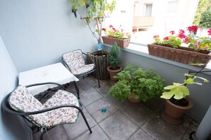 A small patio area with a white table and two chairs, surrounded by potted plants and a small tree. - Hotel Amadeus (Speyer)