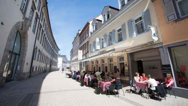 A street with outdoor seating at cafes, buildings with shutters, and a clear sky. - Hotel Amadeus (Speyer)