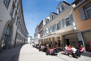 A street with outdoor seating at cafes, buildings with shutters, and a clear sky. - Hotel Amadeus (Speyer)