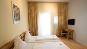 A hotel room with two beds, a desk, a chair, a television, and a window with curtains. - Hotel Amadeus (Speyer)