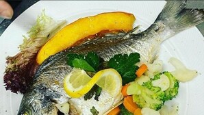 A plate with a whole fish, lemon slices, and mixed vegetables. - Hotel Amadeus (Speyer)