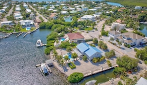Vue aérienne d’un quartier résidentiel situé sur la côte, avec des maisons, un quai et une piscine.