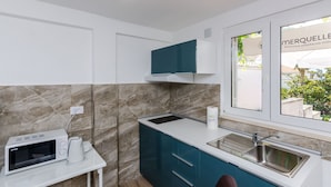 Een moderne keuken met een ingebouwde magnetron, waterkoker, spoelbak en een raam met uitzicht op groen.