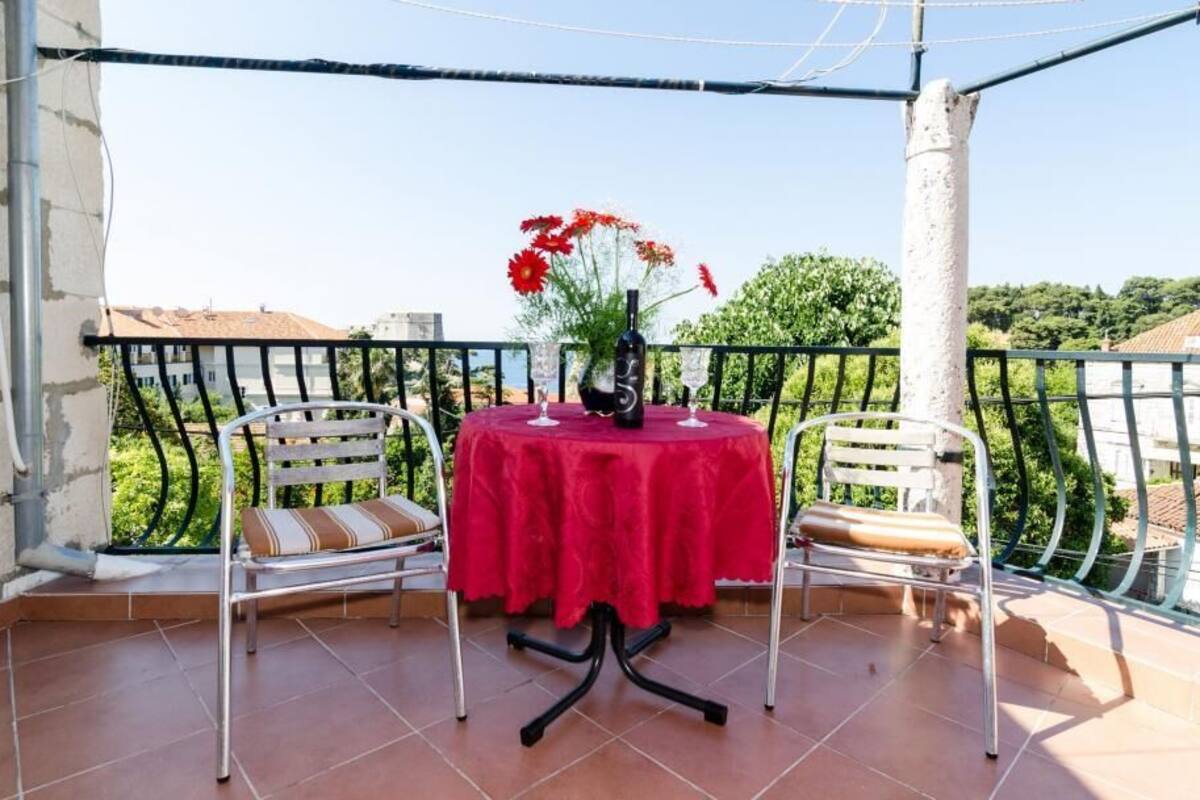 A balcony with a table set for two, a chair, and a vase with flowers.