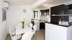 Een moderne keuken met witte kastjes, een eethoek met een witte tafel en stoelen, en een kleine potplant op het aanrecht.