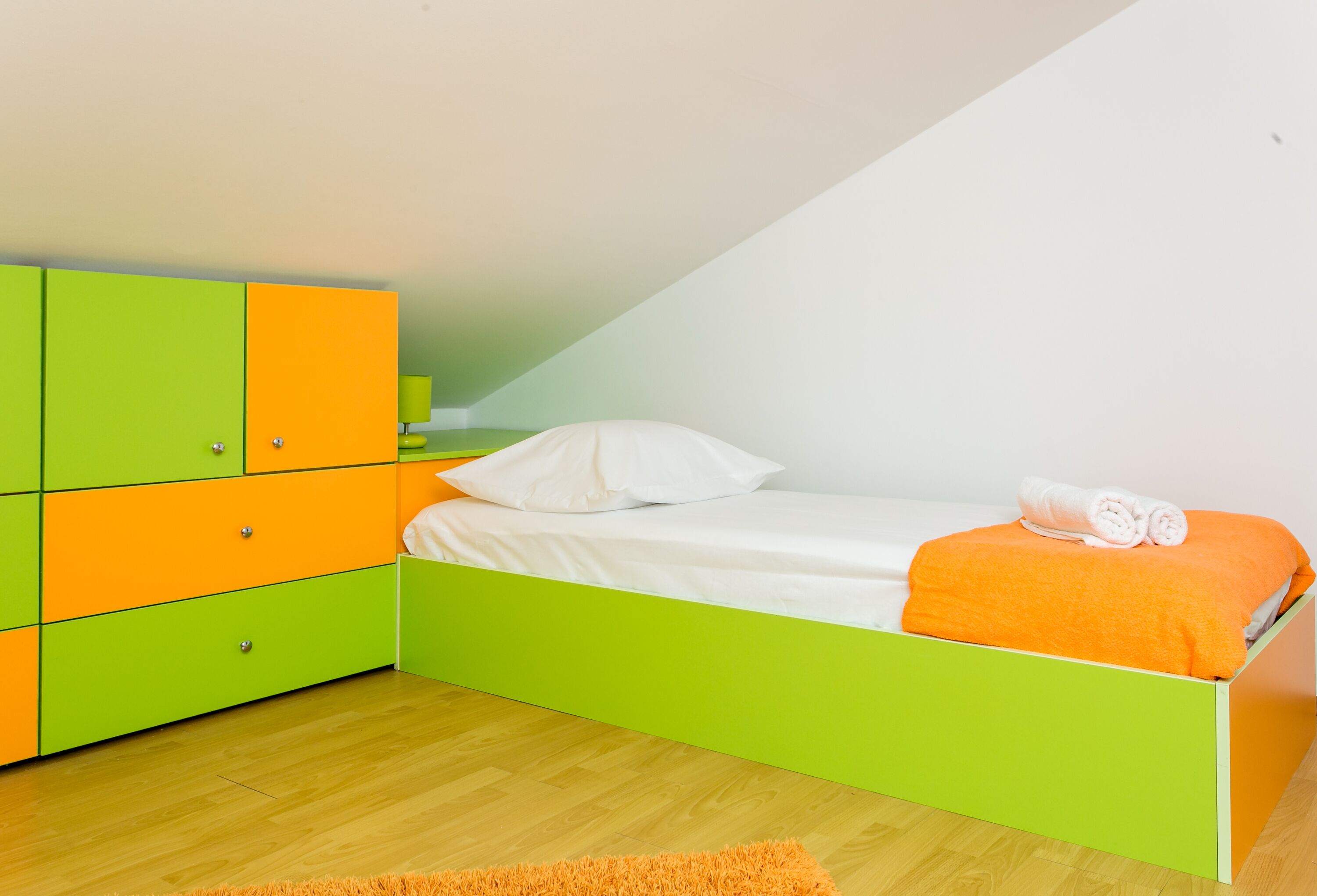 Et soveværelse med en seng i grøn og orange farve, hvidt sengetøj og en grøn garderobe.