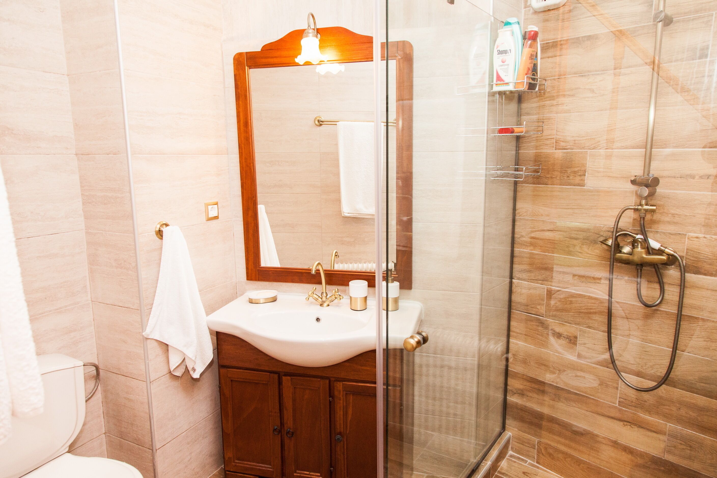 A bathroom with a wooden vanity, a white sink, a mirror, and a glass shower enclosure.