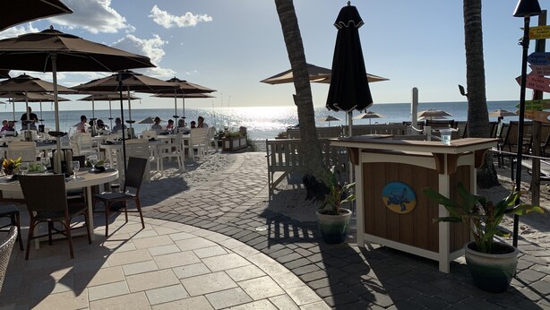 An outdoor dining area with tables and umbrellas, overlooking the beach and ocean. - Minutes to Vanderbilt beach-1/2 mile !! Heated Pool/Spa 2650 sq ft (Naples)