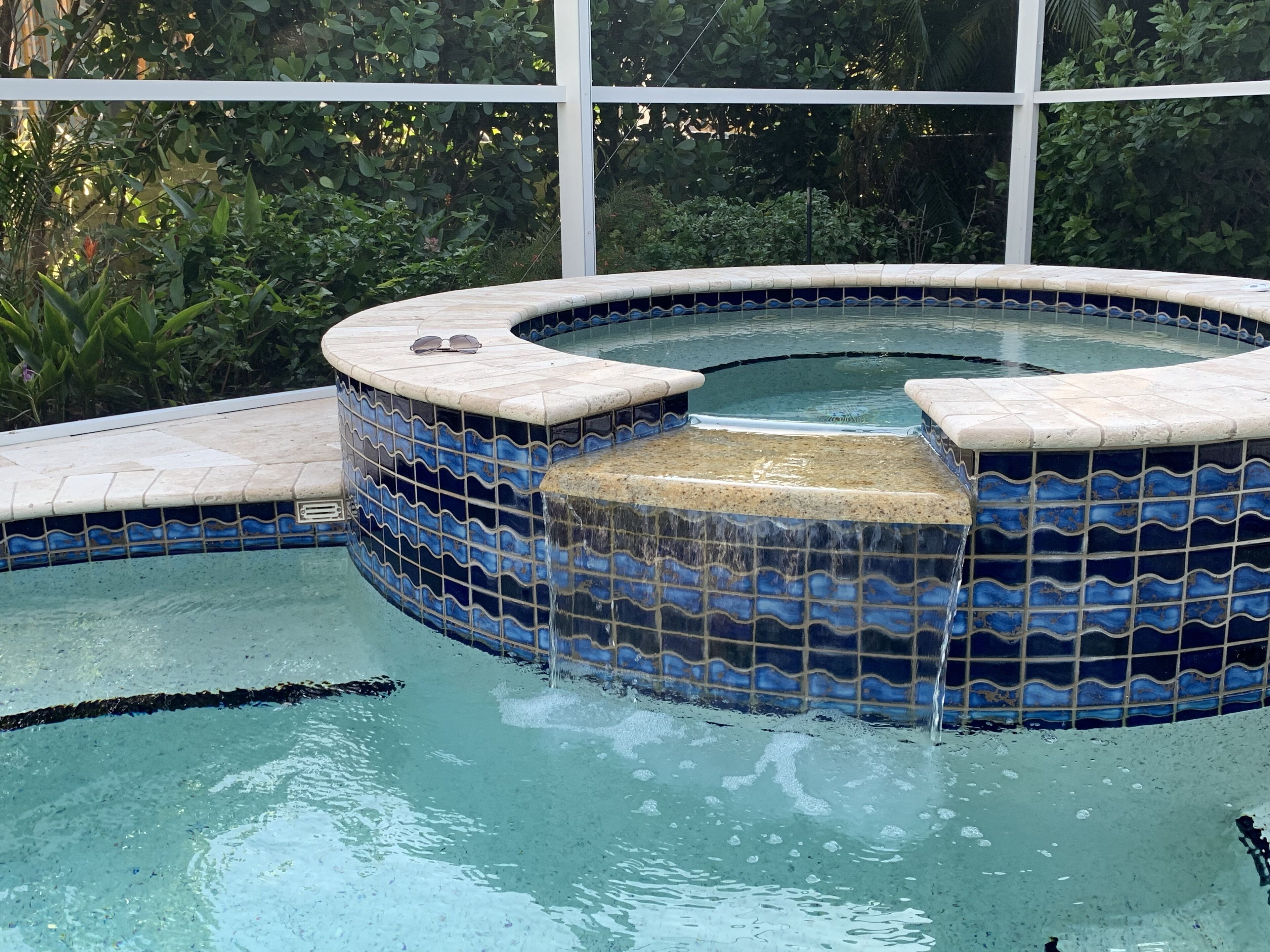 Un jacuzzi con mosaicos azules y blancos, rodeado por una piscina.