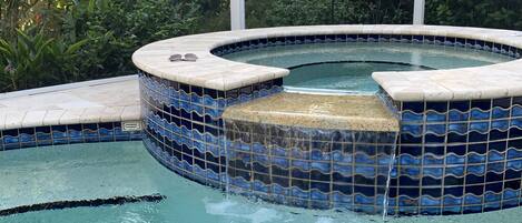 Un jacuzzi con mosaicos azules y blancos, rodeado por una piscina.