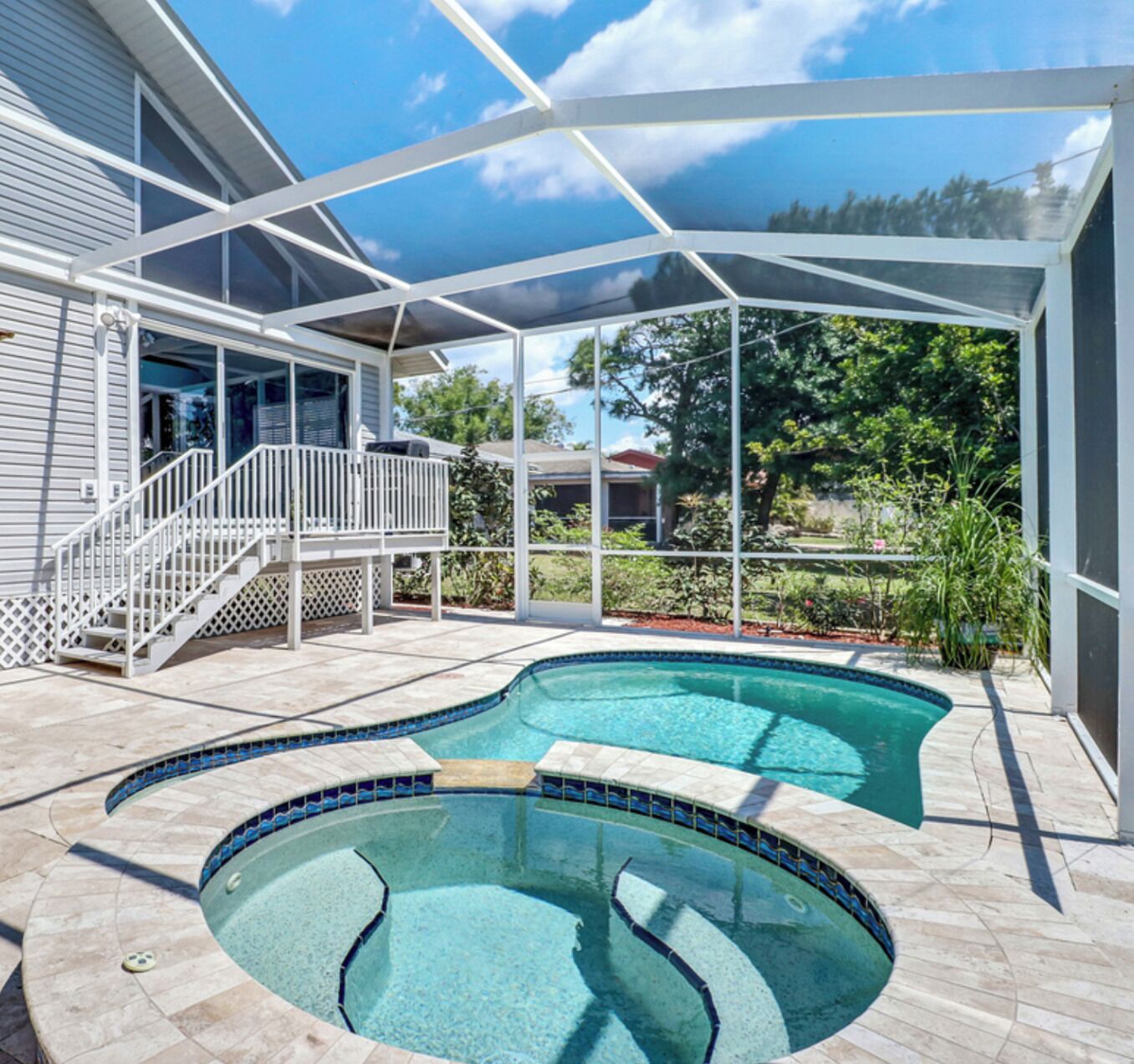 A swimming pool with a glass enclosure, a covered deck, and a staircase leading to a balcony.