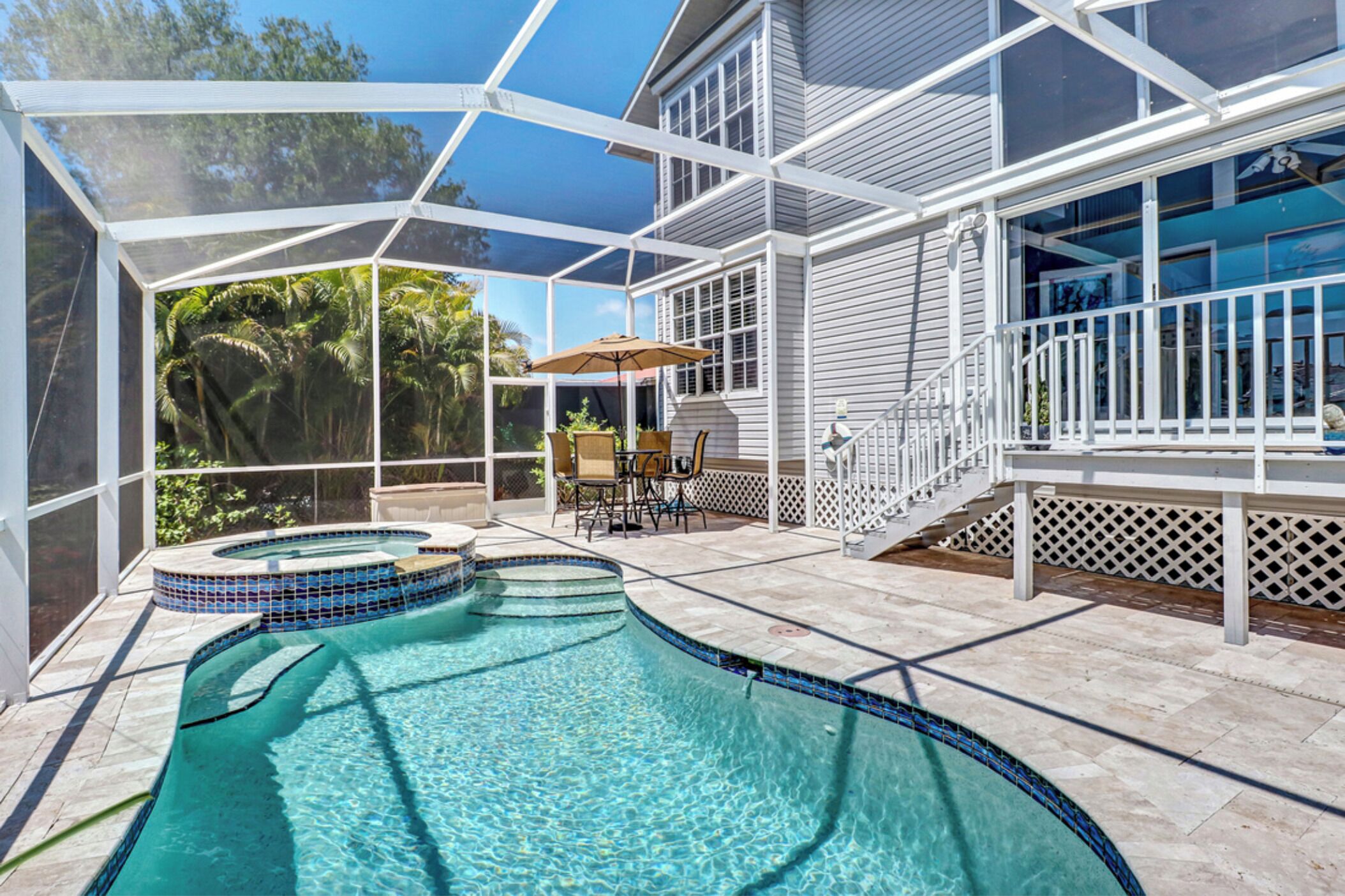 A covered swimming pool with a hot tub, patio furniture, and a view of the surrounding greenery.