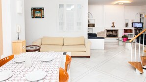 A modern living room with a dining area, a sofa, a fireplace, and a TV. - Apollon Stone Villa in Delphi (Delphi)