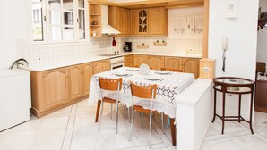 A kitchen with wooden cabinets, a dining table with chairs, a coffee machine, and a telephone. - Apollon Stone Villa in Delphi (Delphi)
