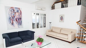 A living room with a dark blue sofa, a beige sofa, a glass coffee table with a pink flower vase, and a painting on the wall. - Apollon Stone Villa in Delphi (Delphi)