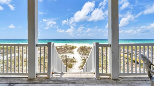 A wooden deck with white railings overlooking a beach path leading to the ocean.
