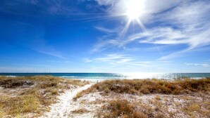 A beach path leading to the ocean with a clear sky and sunlight.