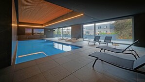 Ein modernes Hallenbad mit Liegestühlen und einer Holzbalkendecke.
