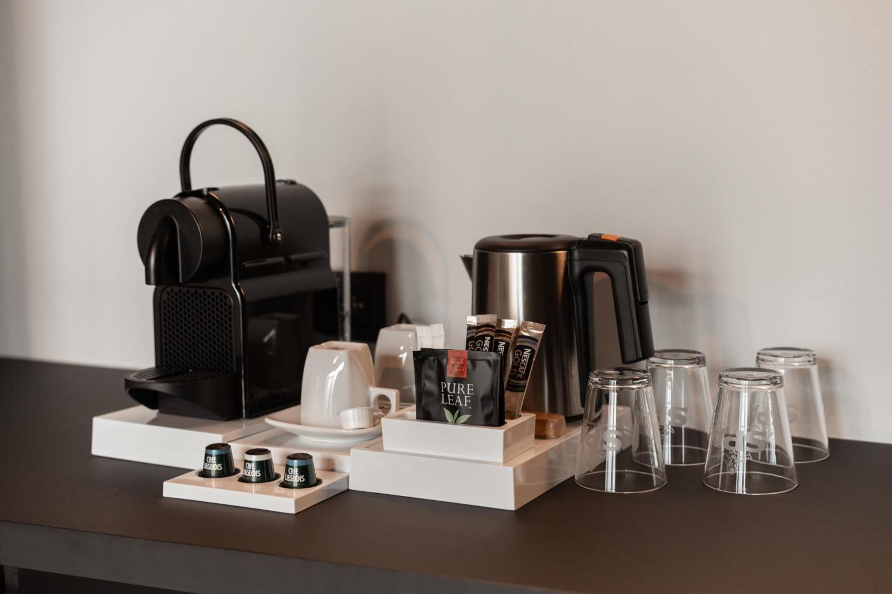 A coffee station with a coffee maker, cups, and coffee pods on a wooden stand.