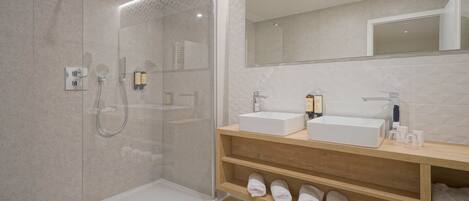 A modern bathroom with a glass-enclosed shower, two sinks, and a wooden vanity with towels.