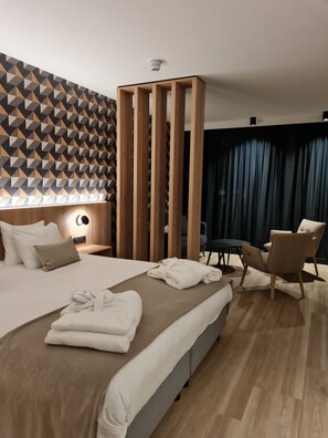 Una habitación de hotel moderna con una cama grande, un separador de madera, un escritorio, una silla y vistas a la ciudad.