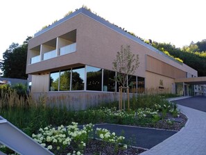 Un edificio moderno con tejado plano, amplias ventanas y un jardín ajardinado con flores blancas.