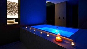Ein modernes Badezimmer mit einer großen Badewanne, einem wandmontierten Spiegel und mehreren beleuchteten Kerzen am Badewannenrand.